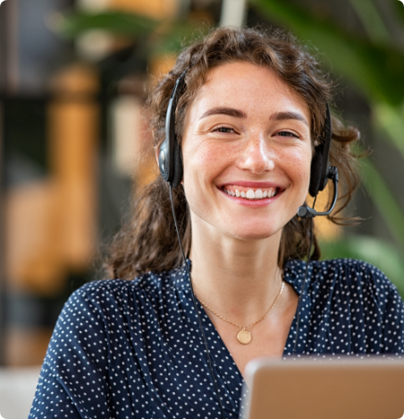 Jeune femme souriante, devant un ordinateur et portant un casque d'écoute avec micro.