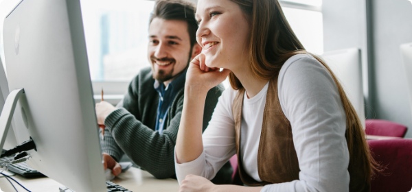 Un homme et une femme regardent un écrans d'ordinateur en souriant.