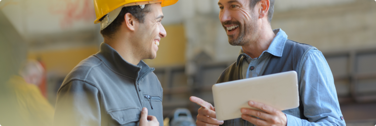 Deux homme sur un chantier parlent et rigole. Un d'eux à une tablette électronique à la main.