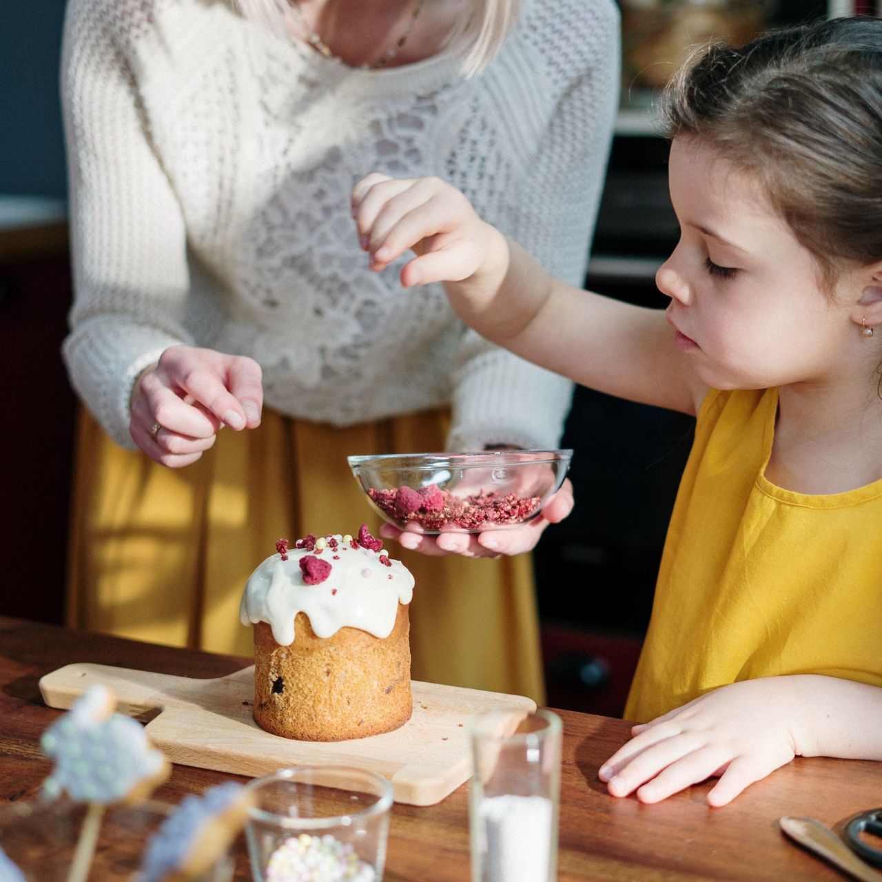 Photo d'une petite fille qui saupoudre des morceaux de framboises sur le crêmage d'un petit gâteau.