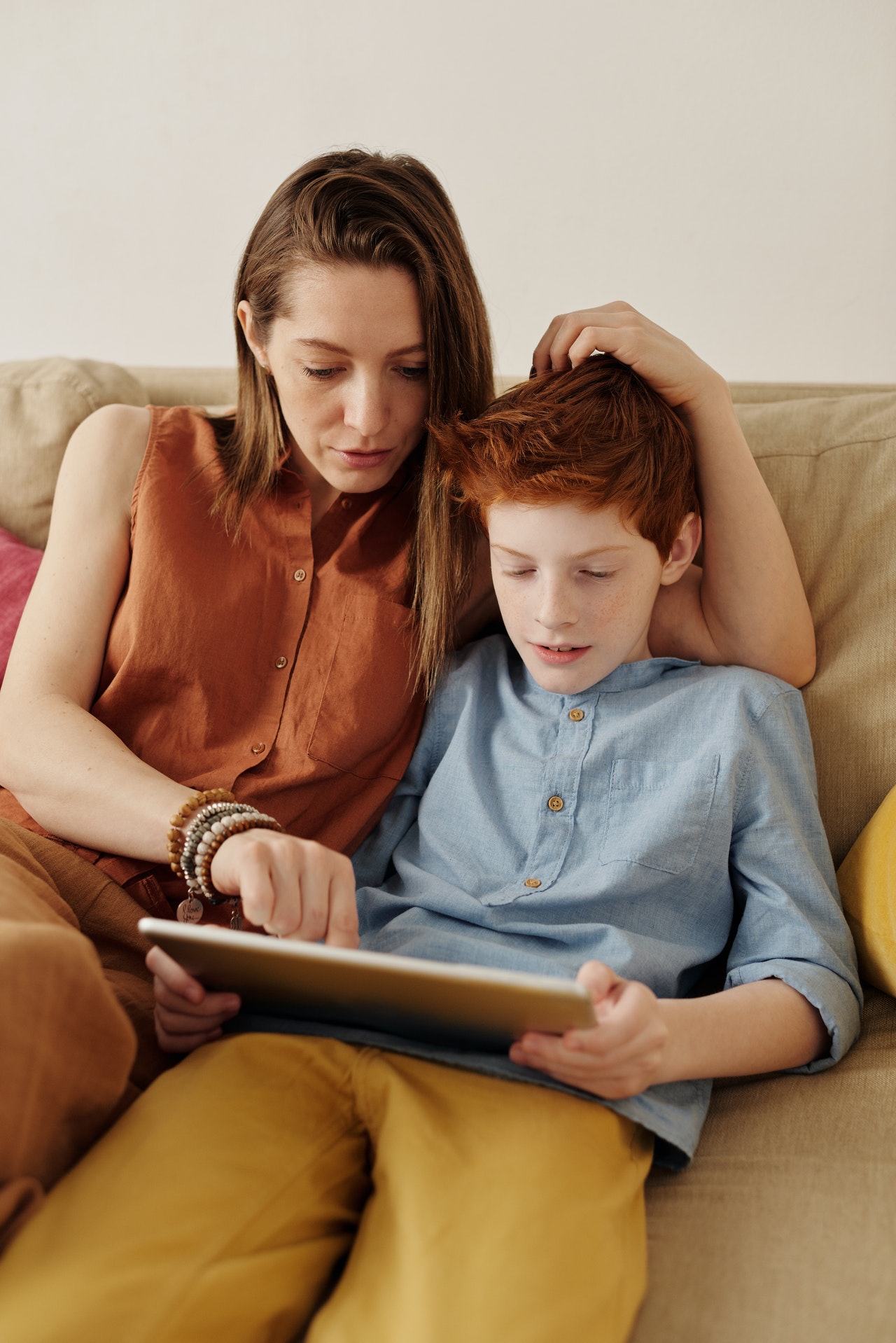 Une mère et son garçon lisent une tablette assis sur un sofa.
