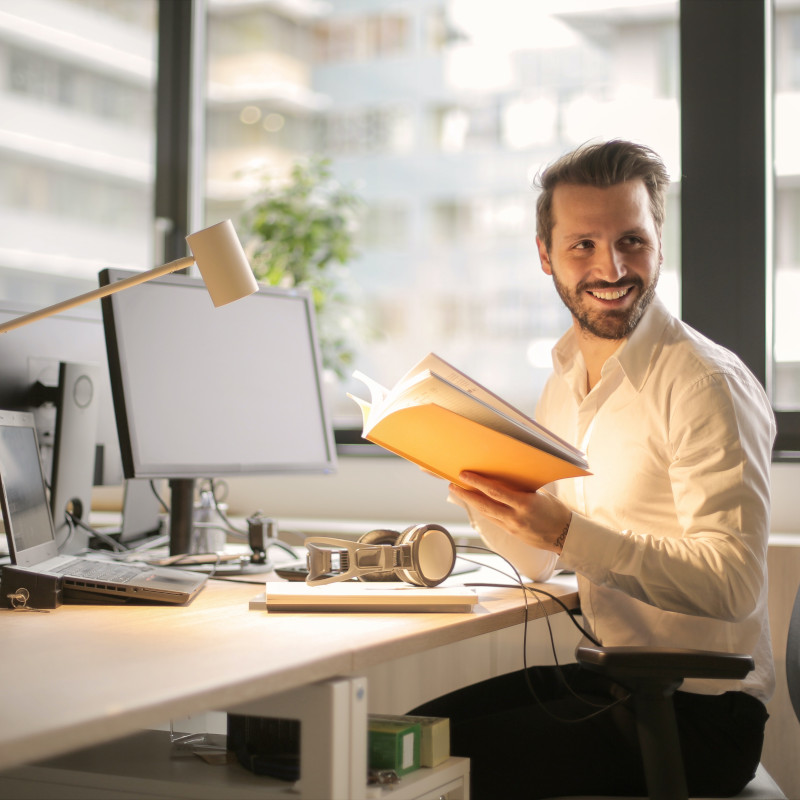 photo d'un homme souriant et tenant un livre devant un bureau.