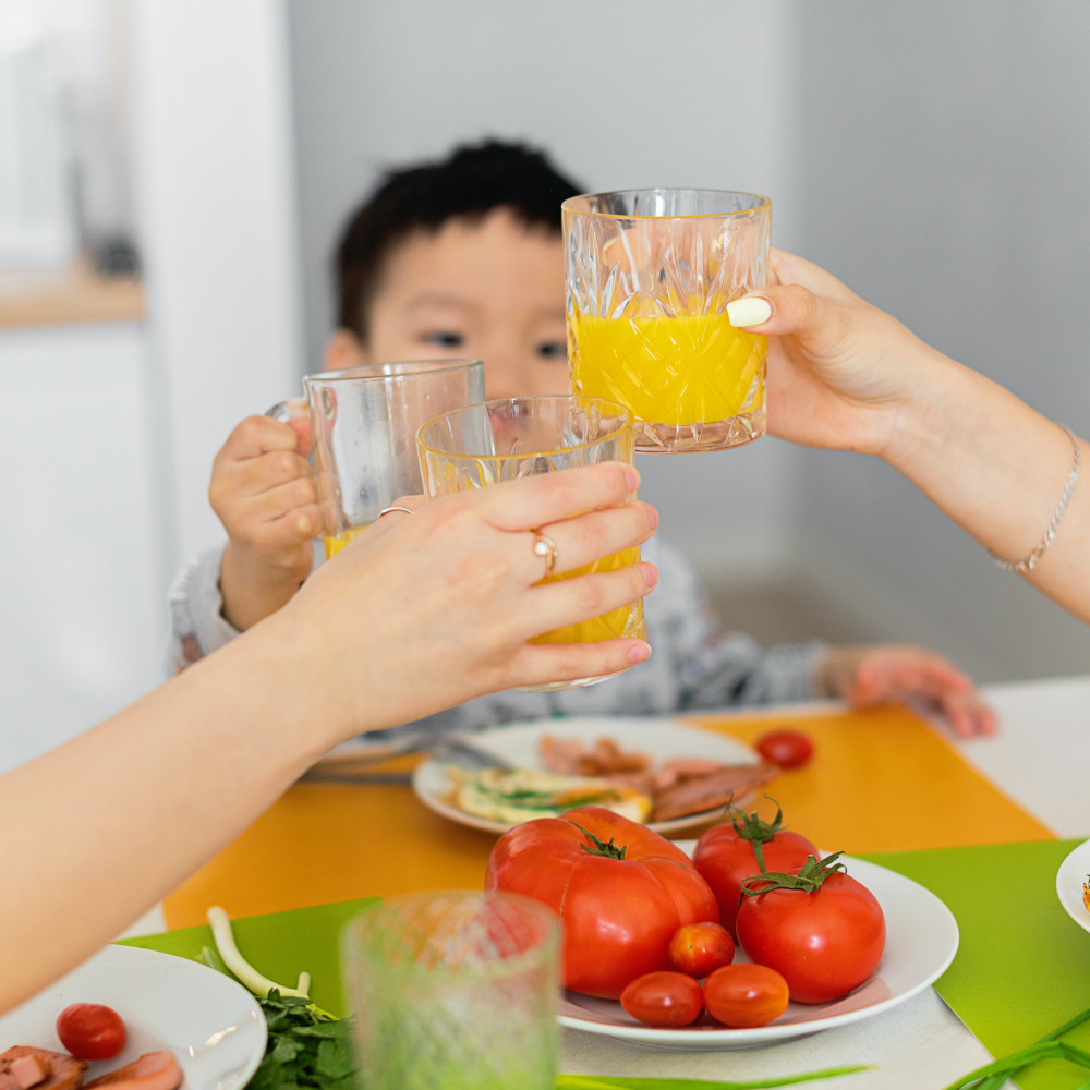 Photo d'un petit garçon qui participe à un toast. En tout, on voit trois verres de jus d'orange.