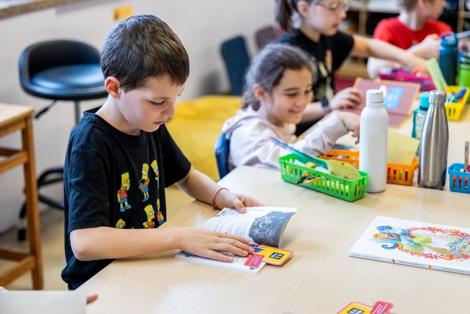 Photo : Une vingtaine d'enfants sont assis sur le plancher. S'eux de la première ligne tiennent chacun un papier avec une lettre épelant "Merci!"