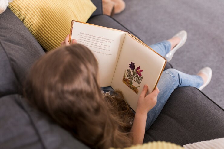 girl-reading-book-couch_23-2147783637 Photo vue aérienne : plusieurs enfants, livre en mains, sont couchés sur le dos et forme un cercle.